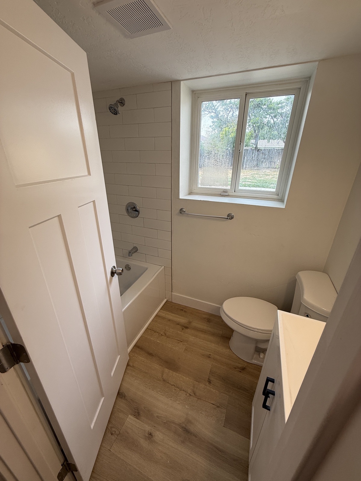 Finished bathroom with an alcove tub and white subway tile surround, a new vanity, LVP floor and a larger clear window