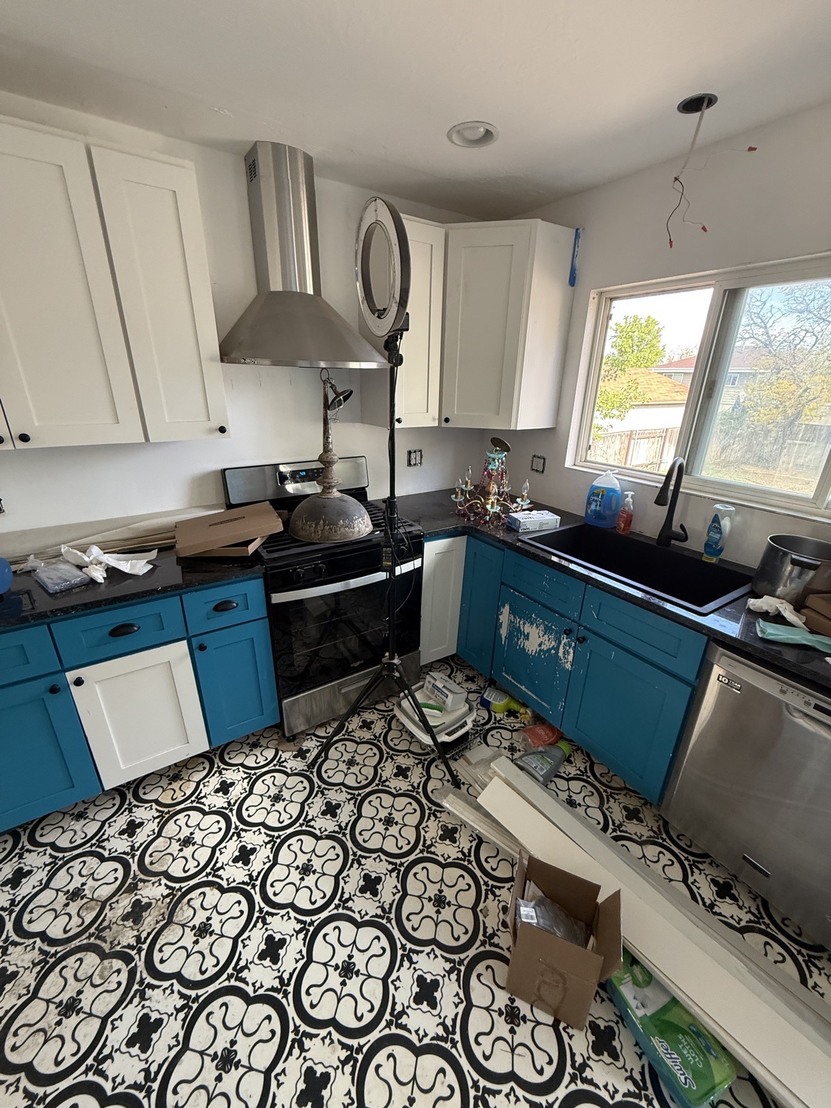 Kitchen part-way through the work: white upper cabinets and dark counters already in, blue lower cabinets and a patterned tile floor still to go