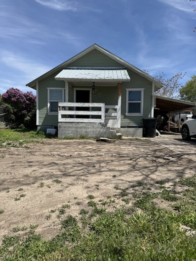 Single-storey house with a bare dirt front yard, patchy weeds and a broken porch rail