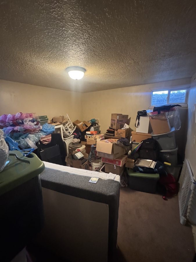 A room filled to window height with cardboard boxes, plastic totes and bagged belongings