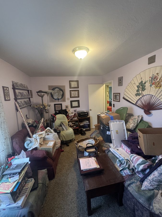 A front room densely furnished and stacked with belongings, boxes and framed pictures