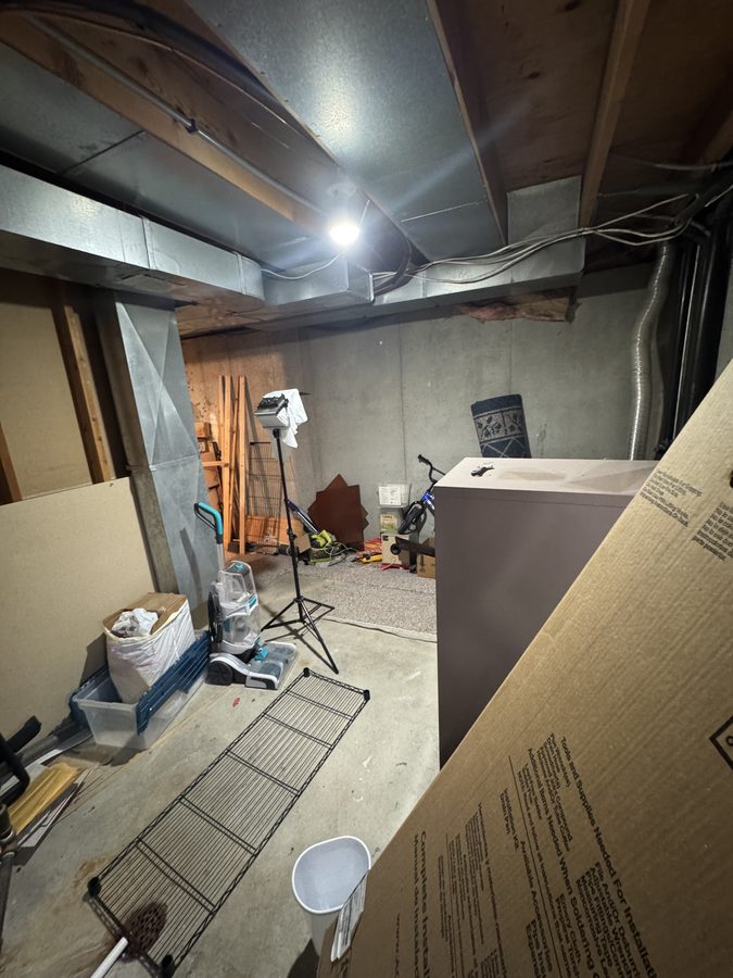Unfinished basement with bare concrete floor, open joists, ductwork and a work light